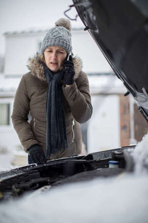 Female Motorist Broken Down In Snow Calling For Roadside Assistance On Mobile Phoneの写真素材