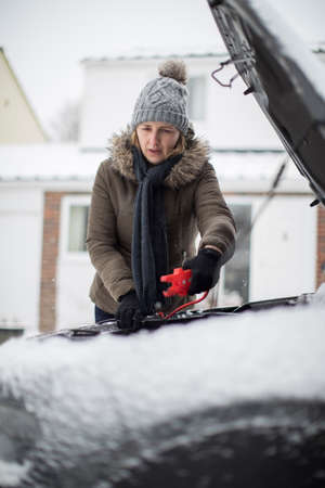 Woman Using Jumper Cables On Car Battery On Snowy Dayの写真素材