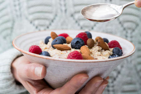 Close Up Of Woman Eating Bowl Of Porridge with Fruit And Nuts For Healthy Breakfast