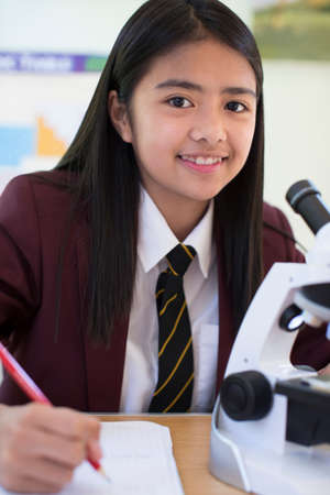 Portrait Of Female Student In Uniform Using Microscope In Science Class