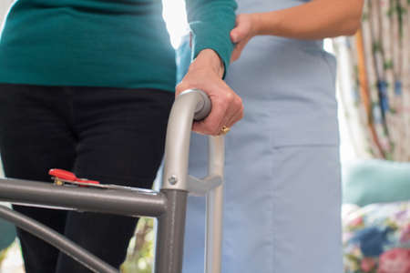 Senior Womans Hands On Walking Frame With Care Worker In Backgroundの写真素材