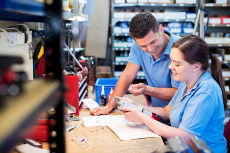 Engineer And Apprentice Examining Component At Workbench