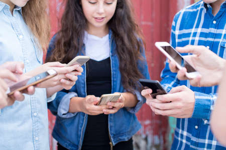 Close Up Of Group Of Teenage Froends Looking At Mobile Phones In Urban Settingの写真素材