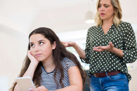 Mother Arguing With Teenage Daughter Over Use Of Mobile Phoneの写真素材