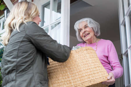 Female Neighbor Helping Senior Woman With Shoppingの写真素材