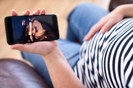Detail Of Pregnant Woman Looking At 3D Image Of Baby On Mobile Phoneの写真素材