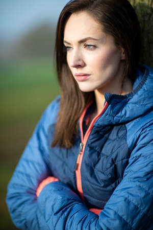 Unhappy Looking Young Woman Leaning Against Tree On Winter Walk In Park