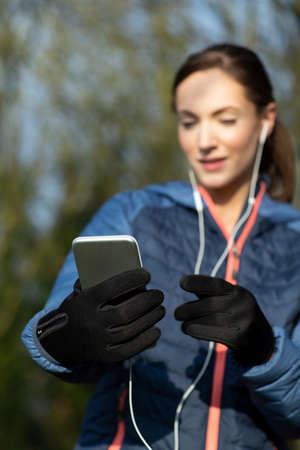 Young Woman Choosing Music To Listen To On Mobile Phone Before Exercising In Park