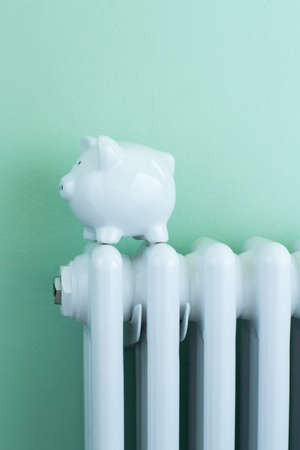 Piggy Bank Balanced On Radiator To Illustrate Energy Costsの写真素材