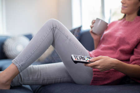 Detail Of Woman Relaxing On Sofa Holding Remote Control And Watching Televisionの写真素材
