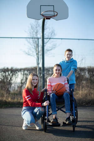 Portrait Of Teenage Girl In Wheelchair Playing Basketball With Friendsの写真素材