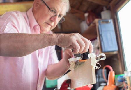 Senior Man Enjoying Carpentry Planing Wood In Garden Shed