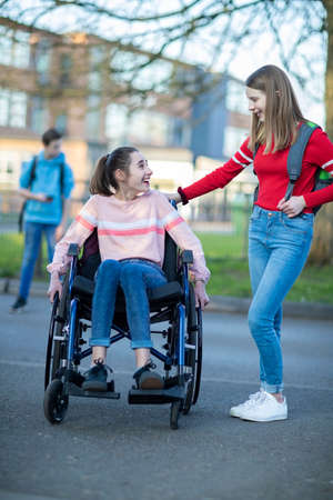 Teenage Girl In Wheelchair Talking With Friend As They Leave High Schoolの写真素材