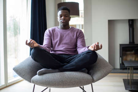 Peaceful Teenage Boy Meditating Sitting In Chair At Homeの写真素材