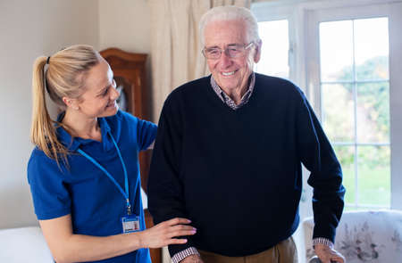 Senior Man Using Walking Frame Being Helped By Care Worker