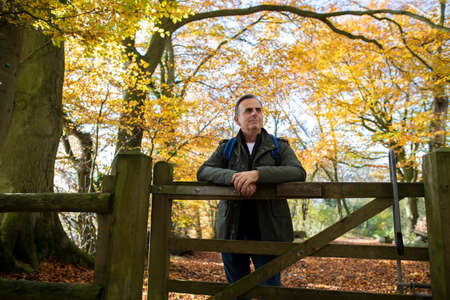 Active Mature Man Leaning On Wooden Gate On Walk Through Autumn Woodland