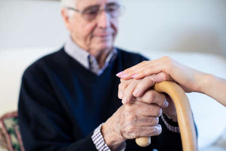 Unhappy Senior Man With Hands On Walking Stick Being Comforted By Woman Health Visitorの写真素材