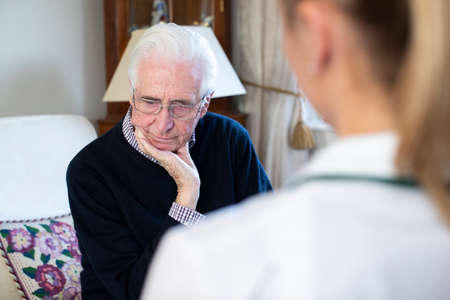Unhappy Senior Man Being Visited By Female Nurseの写真素材