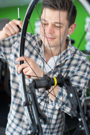 Male Small Business Owner Repairing Wheel In Bicycle Repair Shopの写真素材