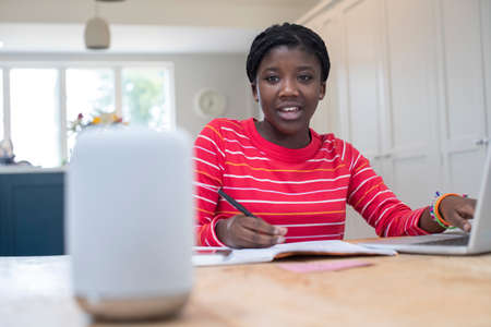 Teenage Girl Doing Homework At Home Asking Digital Assistant Question