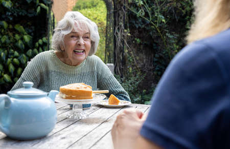 Mature Woman Visiting Lonely Senior Mother In Garden During Lockdown