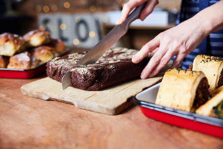 Sales Assistant In Bakery Cutting Freshly Baked Baked Brownies On Counterの写真素材