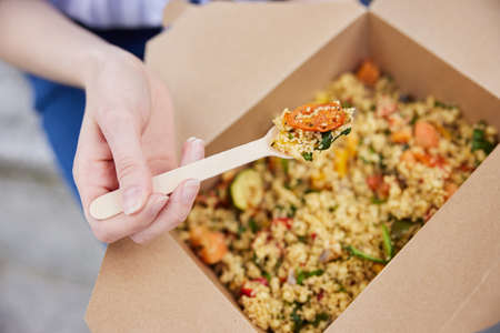 Close Up Of Woman Eating Healthy Vegan Or Vegetarian Takeaway Lunch From Recyclable Packaging With Wooden Forkの写真素材