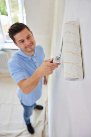 Man Painting Wall In Room Of House With Paint Rollerの写真素材