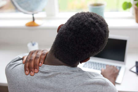 Rear View Of Man At Home Working On Laptop Rubbing Neck And Shoilder in Painの写真素材