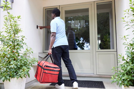 Rear View Of Gig Economy Driver Ringing Doorbell Delivering Online Takeaway Food Order To House