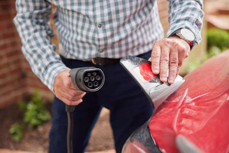 Close Up Of Man Attaching Charging Cable To Environmentally Friendly Zero Emission Electric Car At...