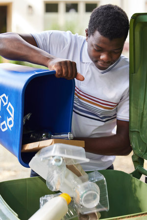 Young Man Emptying Household Recycling Into Green Bin