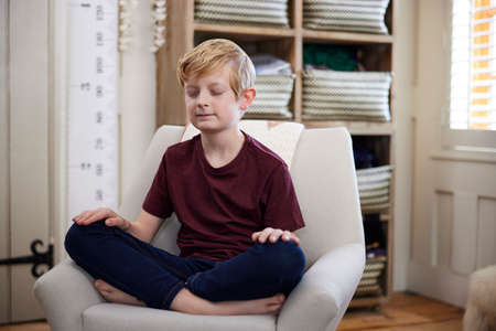 Peaceful Boy Meditating Sitting In Chair In Bedroom At Homeの写真素材