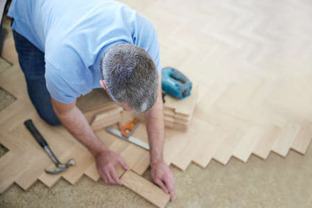 Overhead View Of Carpenter Or Builder Laying New Wood Block Parquet Parquet Floor In Kitchen At Homeの写真素材