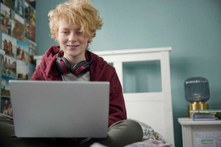 Teenage Girl With Wireless Headphones Working On Laptop In Bedroom At Homeの写真素材