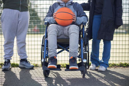Close Up Of Teenage Girl In Wheelchair With Friends Playing Game Of Basketball In Park Togetherの写真素材