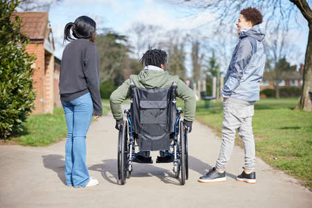 Teenage Boy In Wheelchair Hanging Out Talking And Laughing With Friends In Parkの写真素材