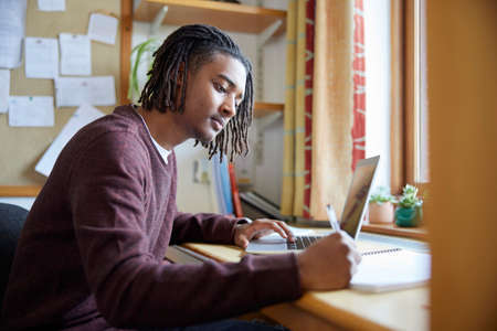 Male University Or College Student Studying With Laptop At Desk In Roomの写真素材