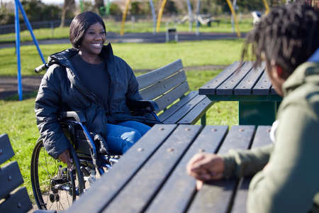 Teenage Girl In Wheelchair Hanging Out Talking And Laughing With Friends In Parkの写真素材