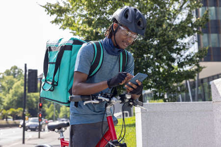 Courier On Bike Delivering Takeaway Food In City Checking Directions And Order Details On Mobile Phoneの写真素材