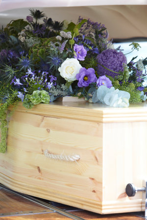 Close Up Of Plain Wooden Coffin With Floral Tributes In Back Of Hearse At Funeralの写真素材