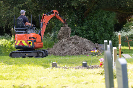 Man Digging Grave In Churchyard Ready For Funeral Small With Automated Diggerの写真素材
