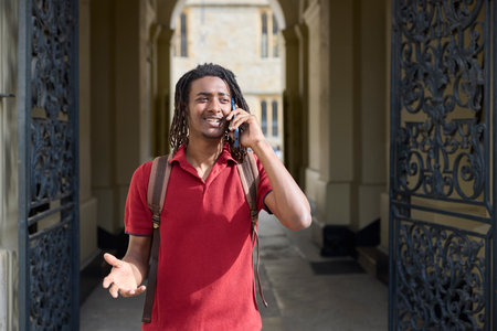 Male Student Making Call On Mobile Phone Outside University Building In Oxford UKの写真素材