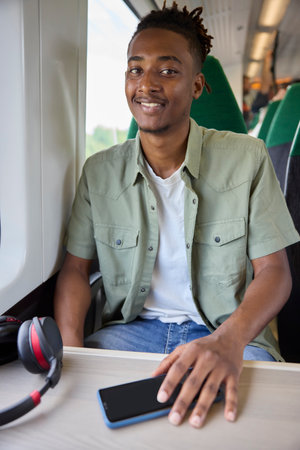 Portrait Of Young Man Commuting To Work Sitting  On Train With Wireless Headphones And Mobile Phoneの写真素材
