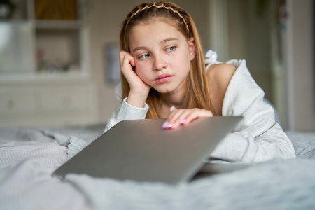 Unhappy Teenage Girl Closing Laptop Lying On Bed At Home Anxious About Social Media Online Bullying And Being Online Too Muchの写真素材