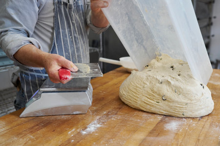 Close up of baker preparing to cut and weigh batch of dough to make individual loaves in bakery