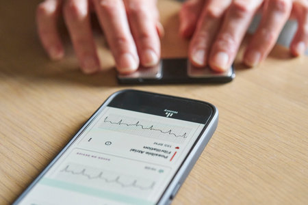 Close up of woman using wireless monitor and app on phone to check heart rateの写真素材