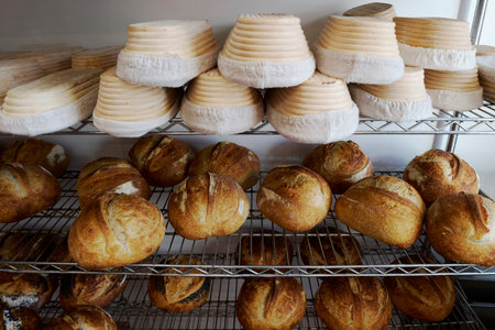 Freshly baked sourdough loaves cooling on racks in bakery with banneton baskets for proving above