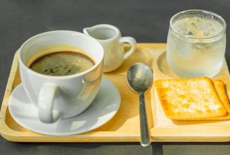 Hot Americano coffee on a wooden tray with crackers and cold water.の写真素材
