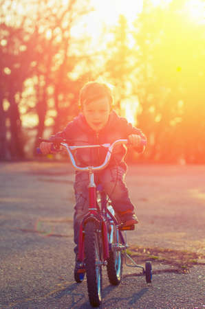Little boy on a bicycle racing towards his goal against the background of the backlight. Vintage compositionの写真素材